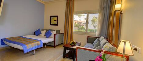 A hotel room with a bed, a sofa, a small table with a vase of flowers, and a lamp.