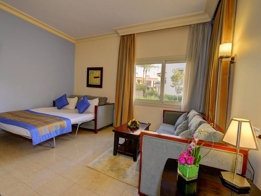 Una habitación de hotel con cama, sofá, una mesita con un florero y una lámpara.