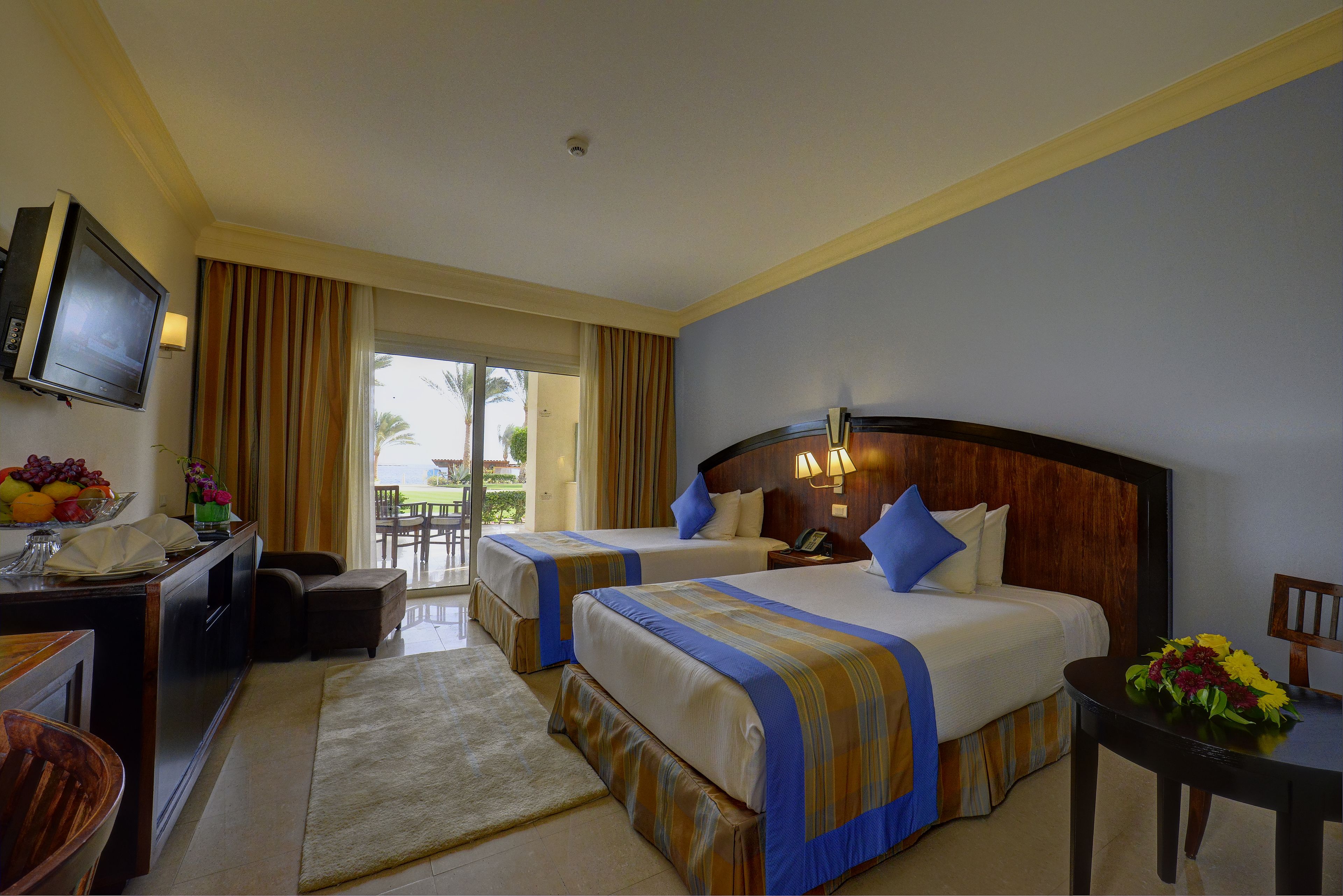 Habitación de hotel con dos camas, un televisor, un escritorio con ordenador y vistas al exterior.