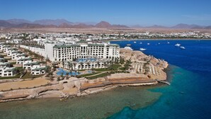 Een kusthotel met zwembad, strand en helderblauw water.