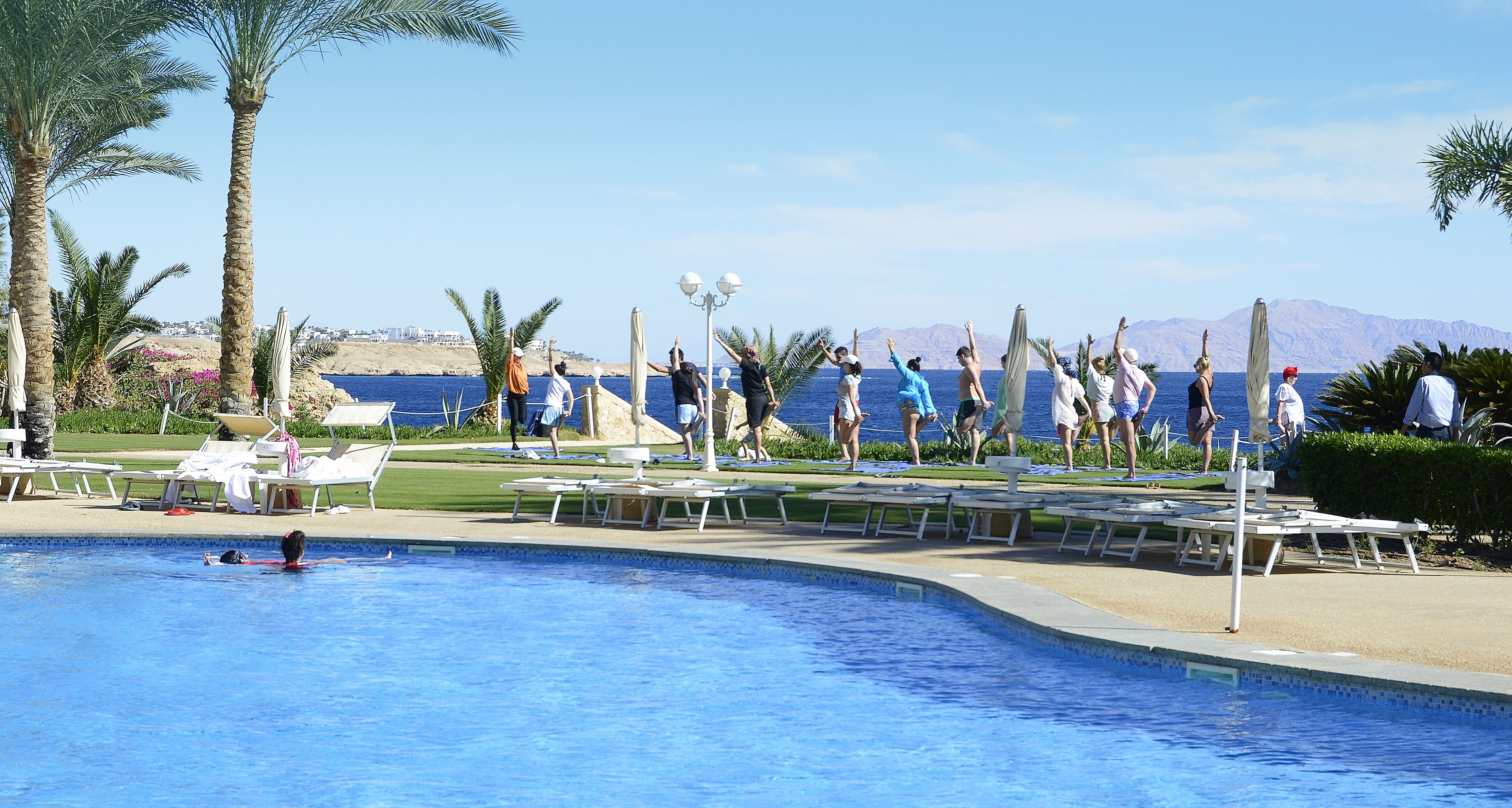 A pool area with lounge chairs and a view of the sea.