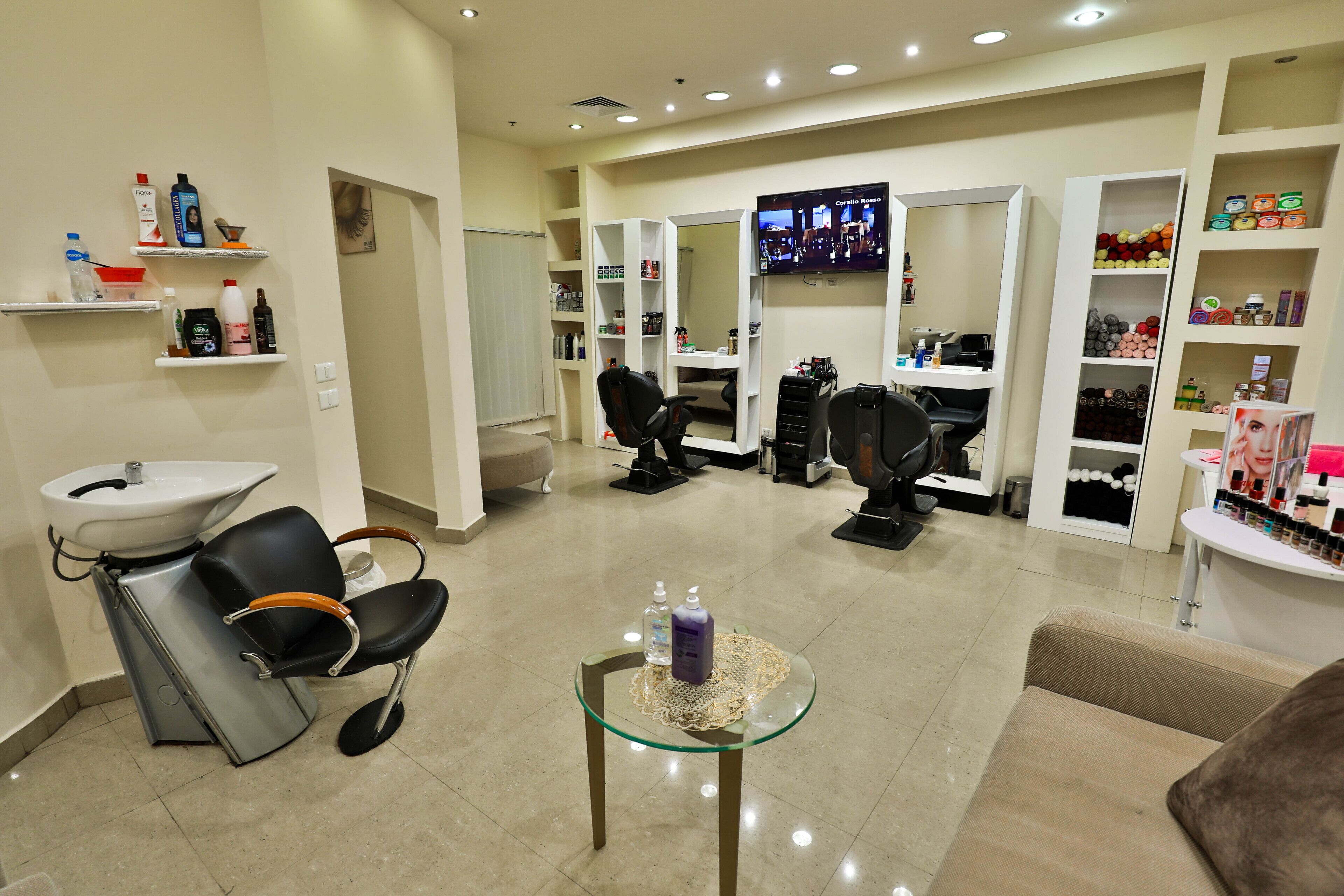 A salon with a sink, two chairs, shelves with hair products, and a TV on the wall.