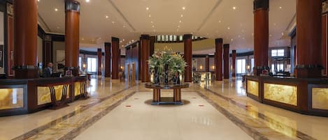 A spacious lobby with marble flooring, a central floral arrangement, and a reception desk.