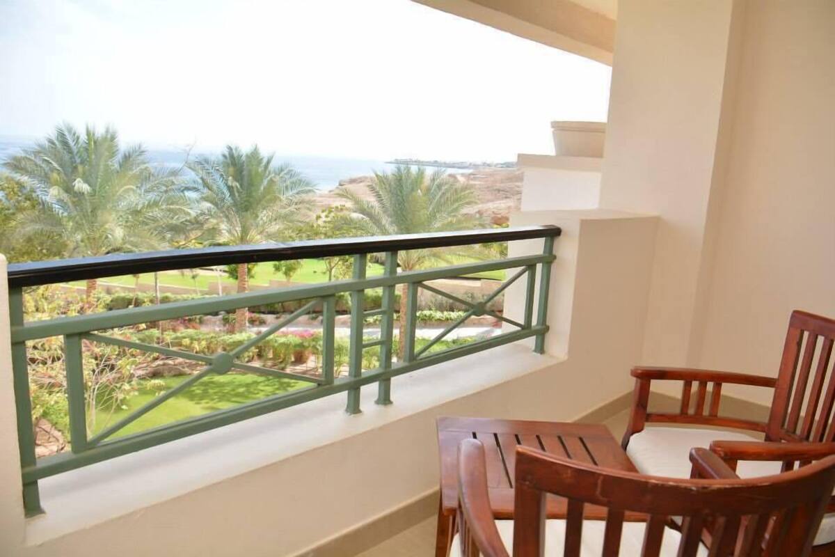 Un balcón con una silla y una mesa de madera, con vista a un jardín ajardinado y al océano.