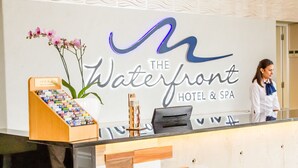 A reception desk at The Waterfront Hotel & Spa with a sign, a flower arrangement, and a display of brochures. - The Waterfront hotel & spa by Misty blue hotels (Durban)