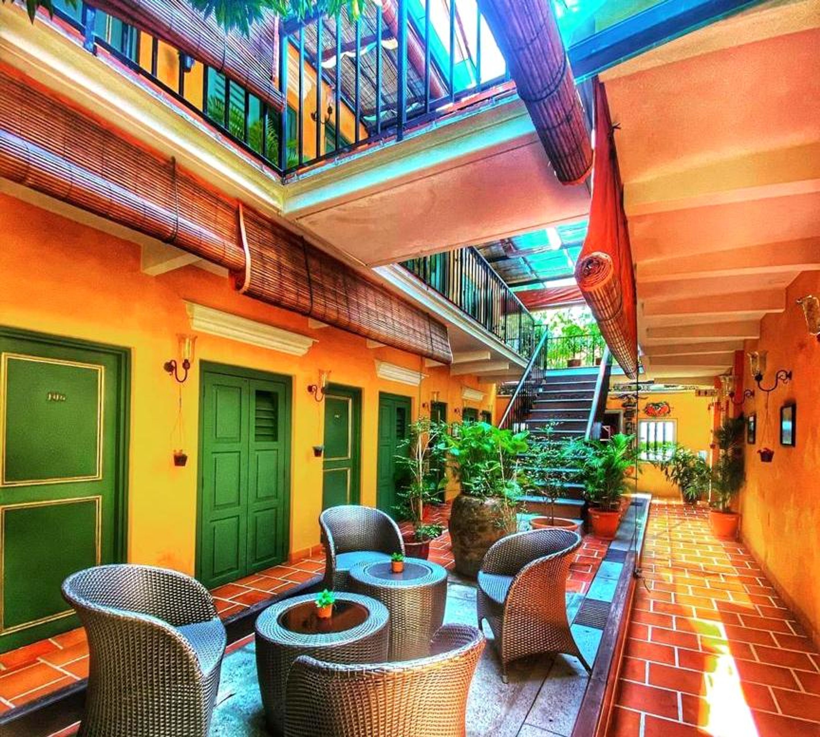 A courtyard with wicker furniture, green doors, and a staircase leading to an upper level.