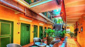 A courtyard with wicker furniture, green doors, and a staircase leading to an upper level.