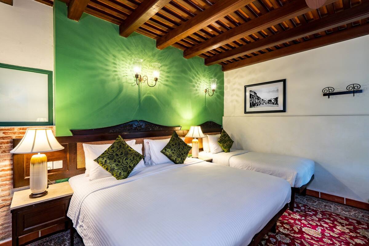 A hotel room with a large bed, two bedside tables with lamps, a green accent wall, a framed picture, and a wooden ceiling.
