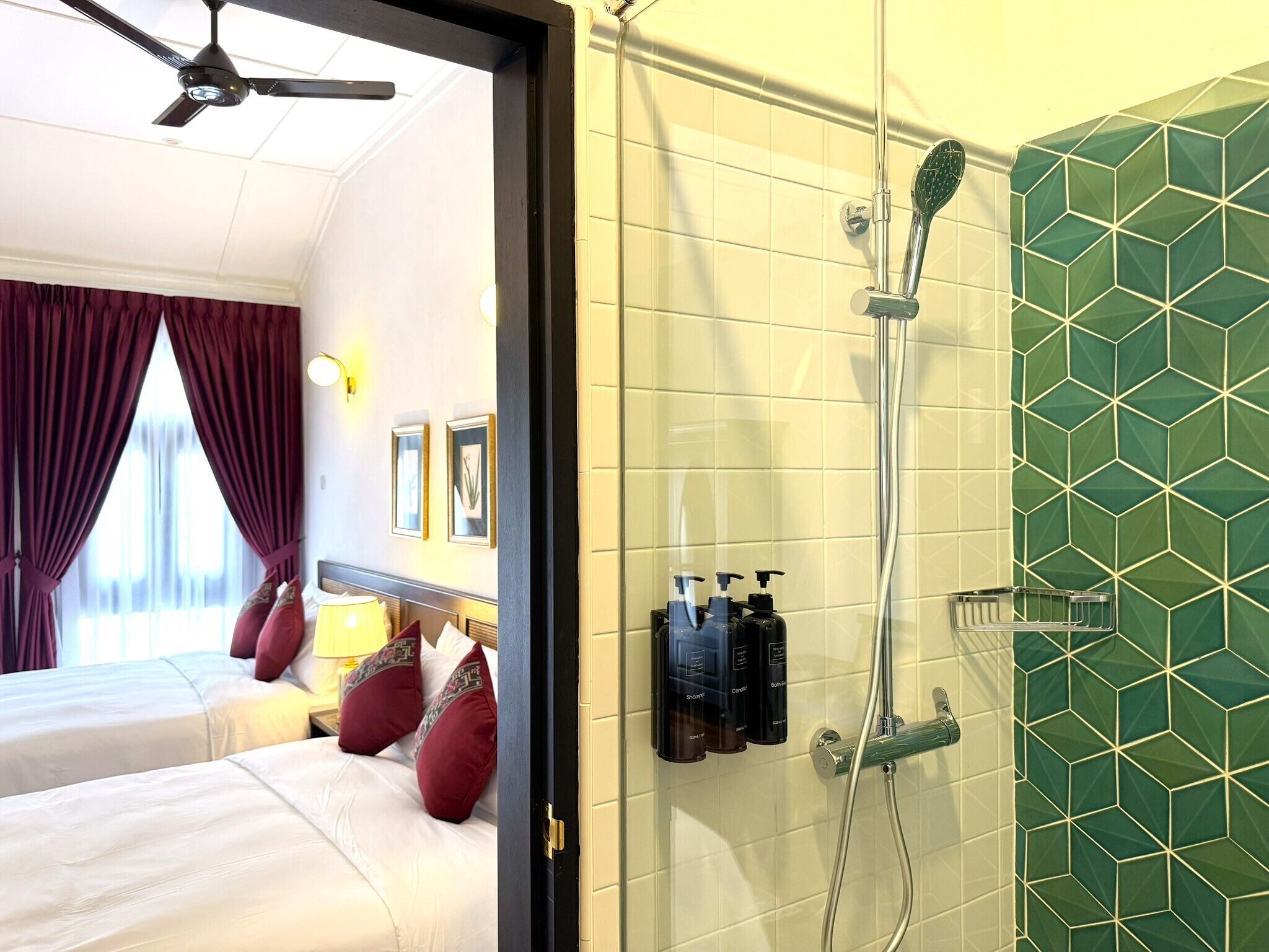 A hotel room with two beds, a shower, and a green-tiled wall.