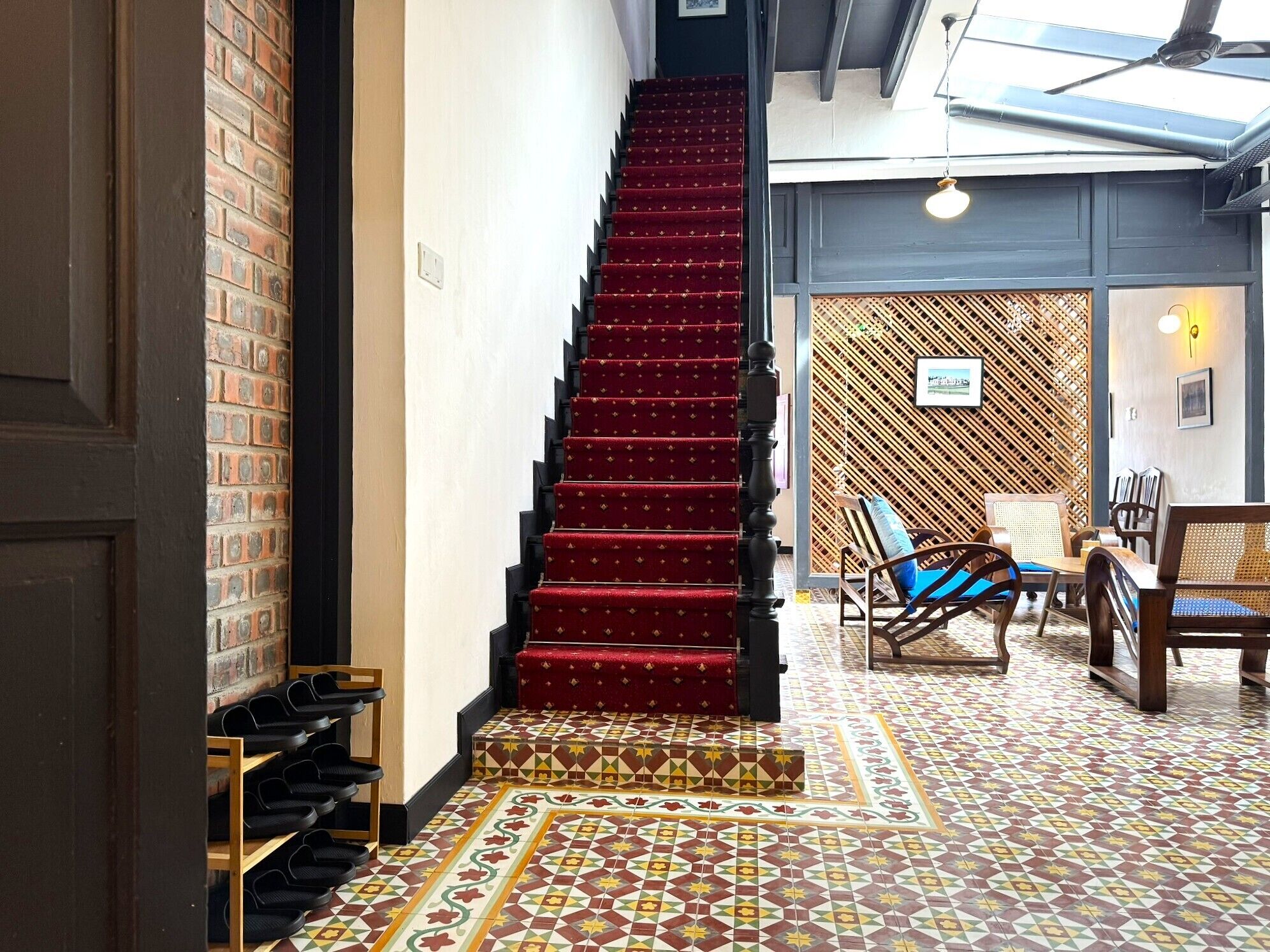 A staircase with red carpet leading to a room with patterned floor tiles, a wooden shoe rack, and a seating area with chairs and a table.