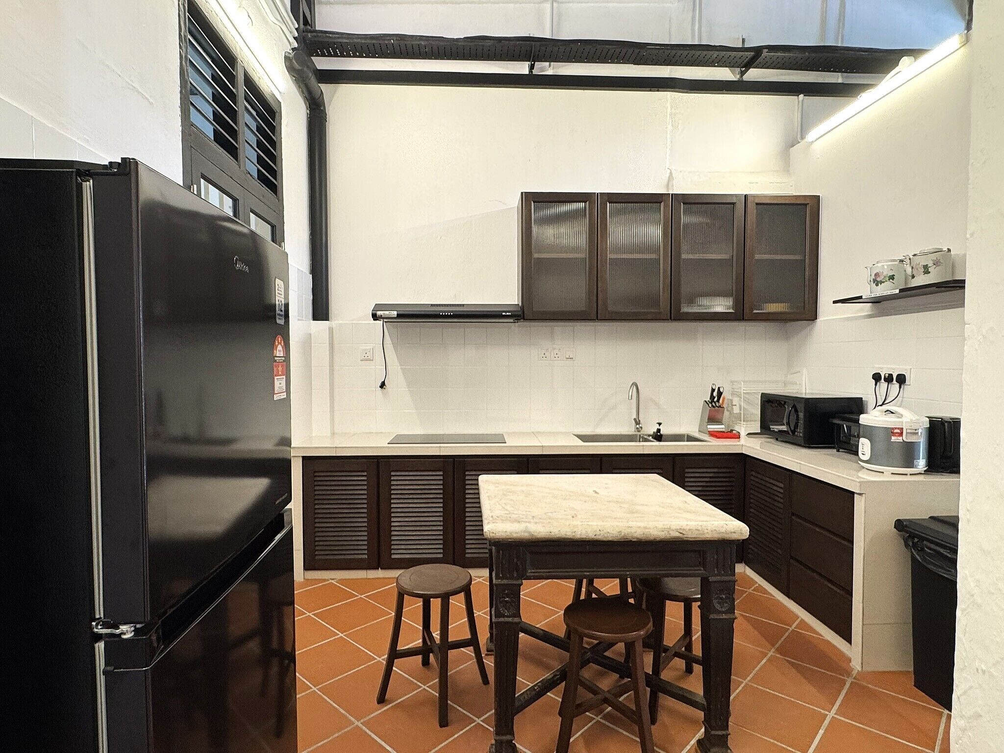 A compact kitchen with a black refrigerator, a sink, a microwave, and a small table with stools.