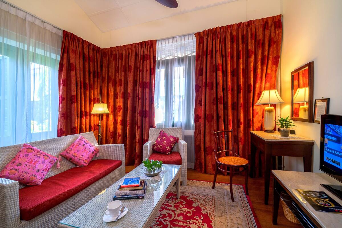 A hotel room with a sofa, armchair, dining table, and a TV.