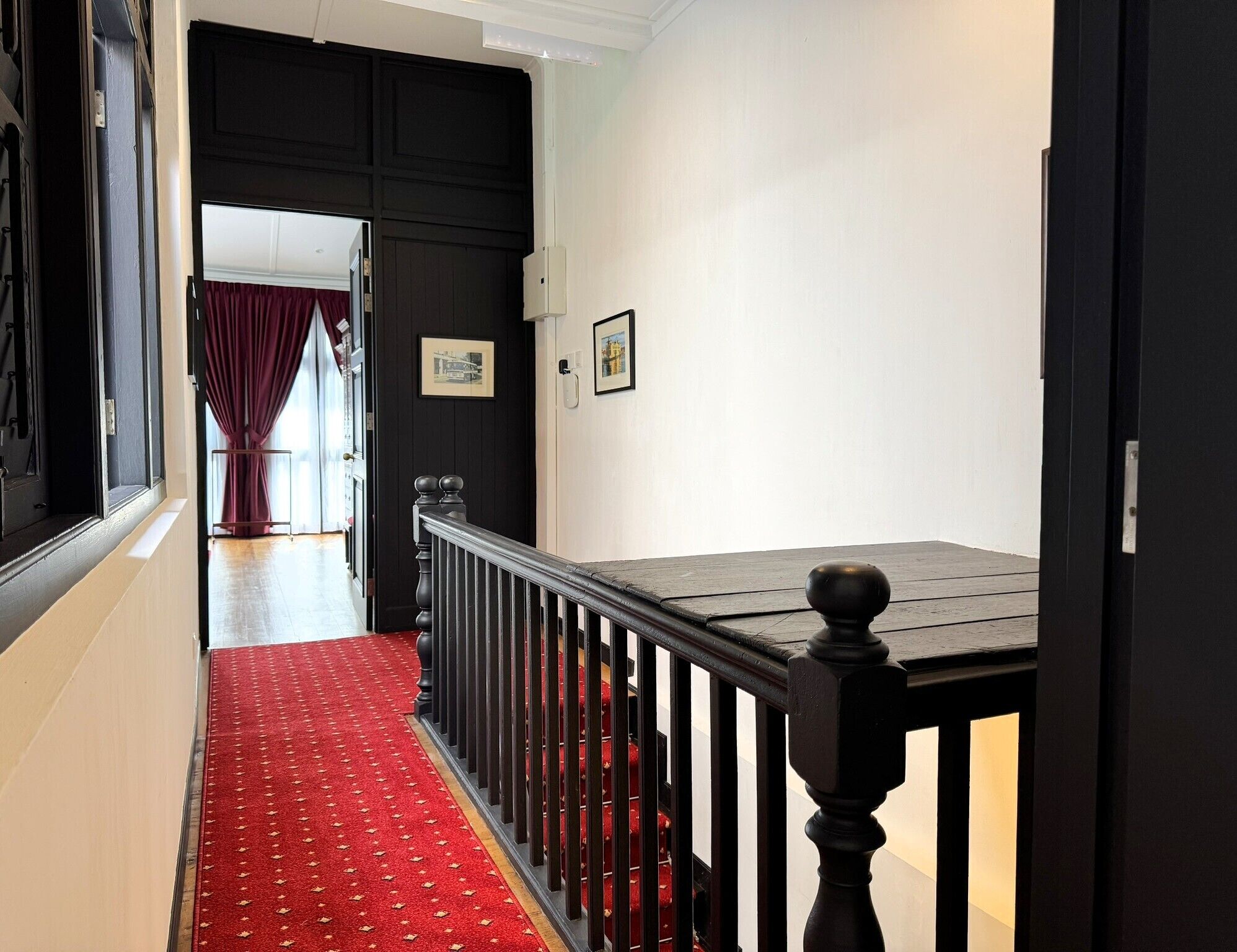 A hallway with a red carpet, black railing, and a door leading to a room with a red curtain.