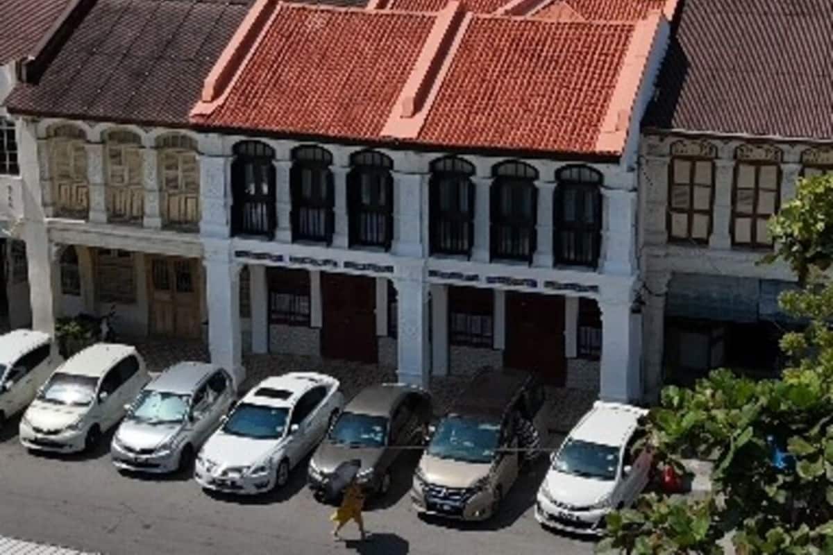 A row of white buildings with red-tiled roofs, parked cars, and a pedestrian.
