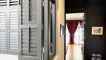 A hallway with a red carpet, a dark wooden door with a picture frame, and a window with red curtains.
