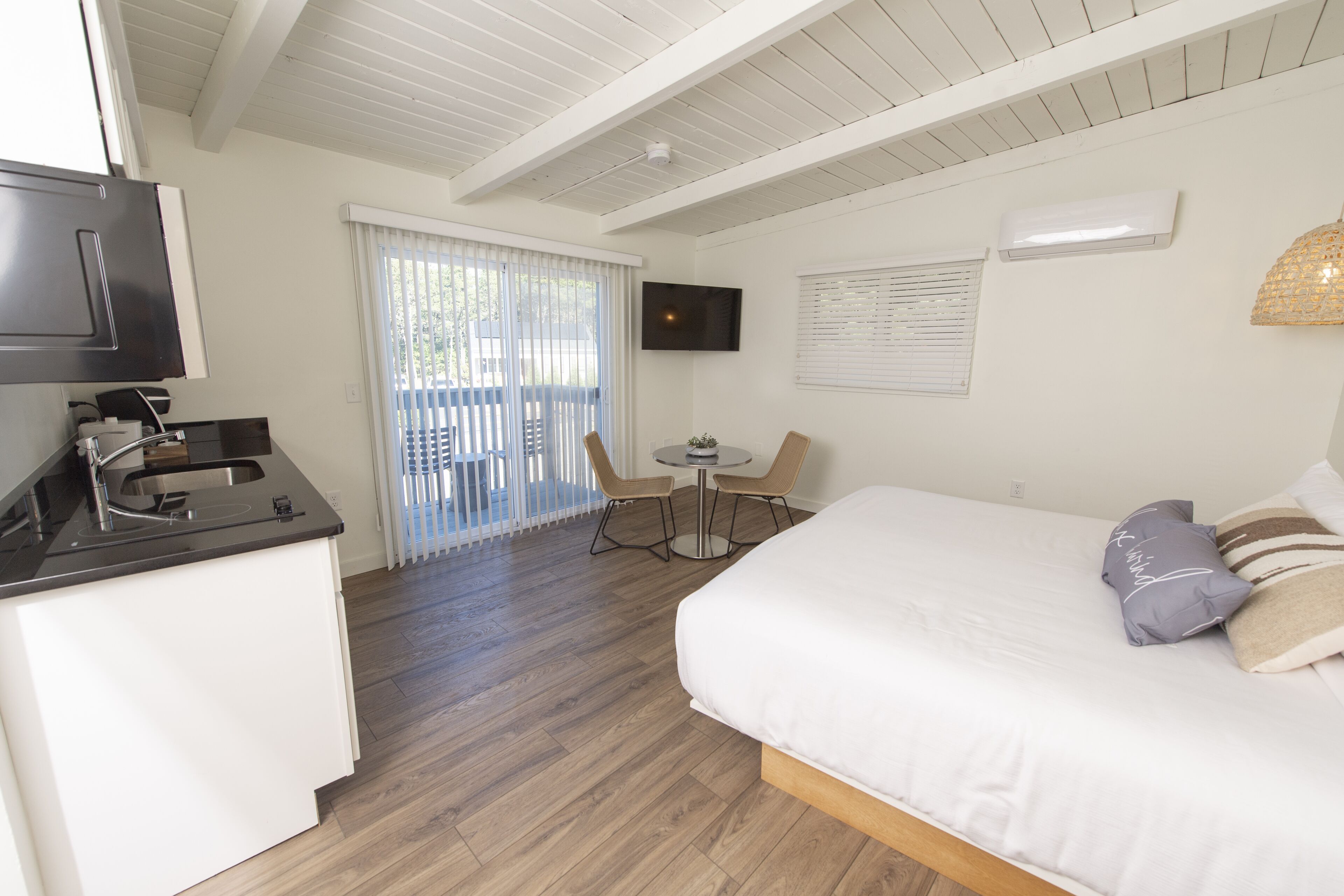 Quarto de hotel com cama, escrivaninha pequena com pia, televisão e varanda com vista.