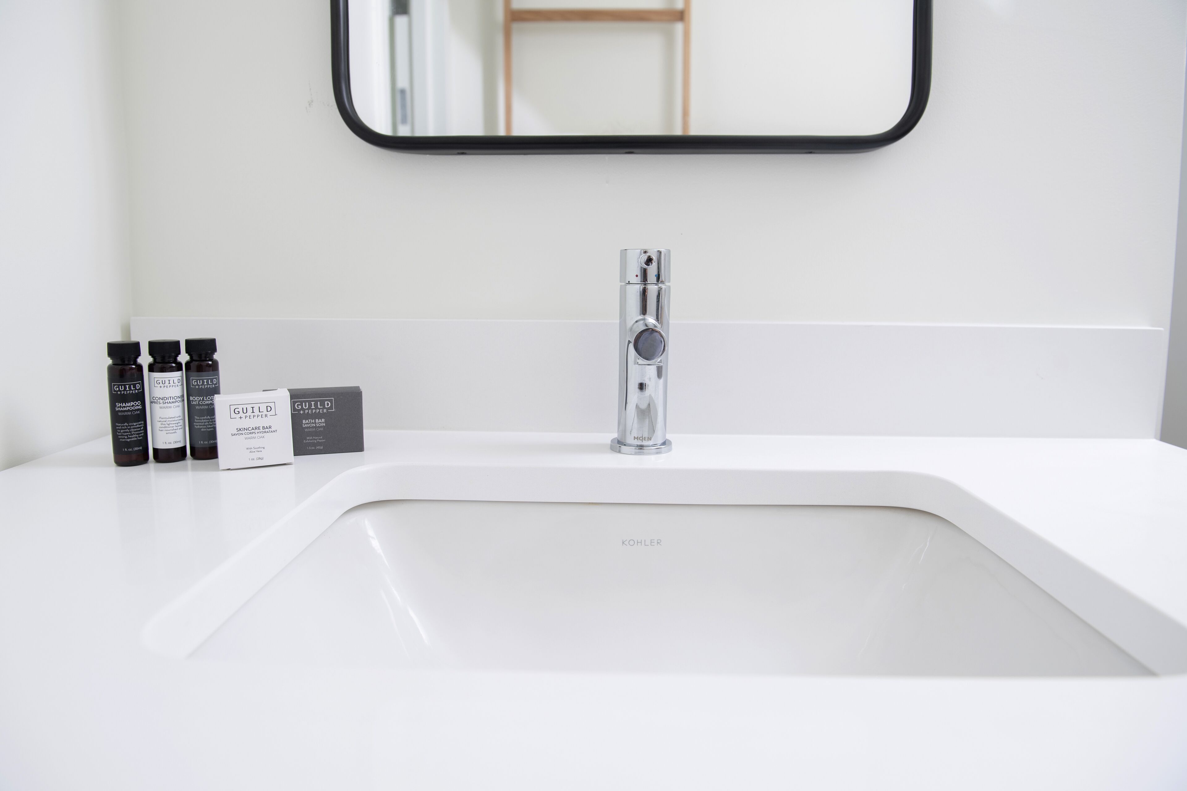 A modern bathroom with a white sink, a chrome faucet, and three bottles of shampoo and conditioner.