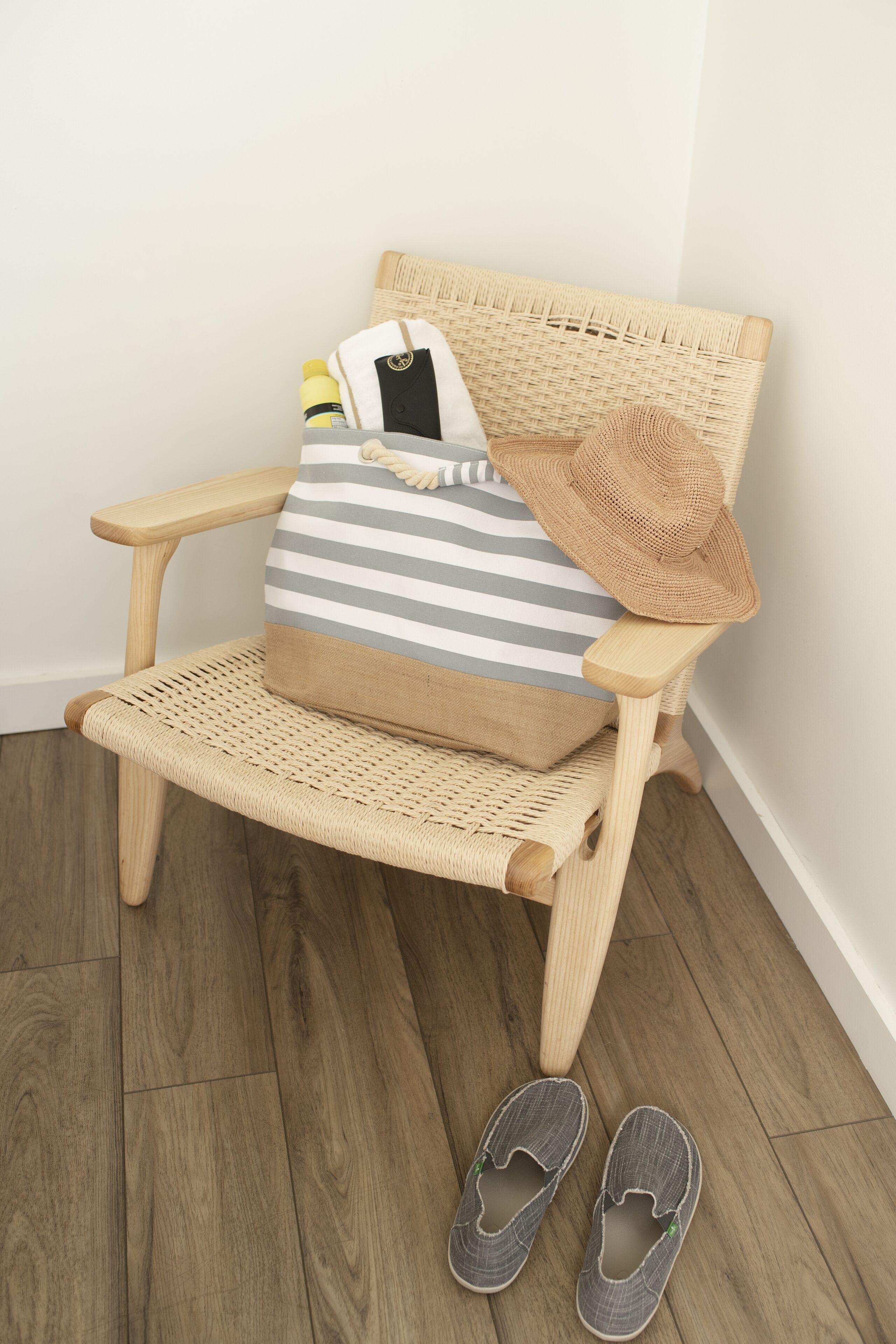 A wicker chair with a striped cushion and a hat, accompanied by a pair of slippers on the floor.