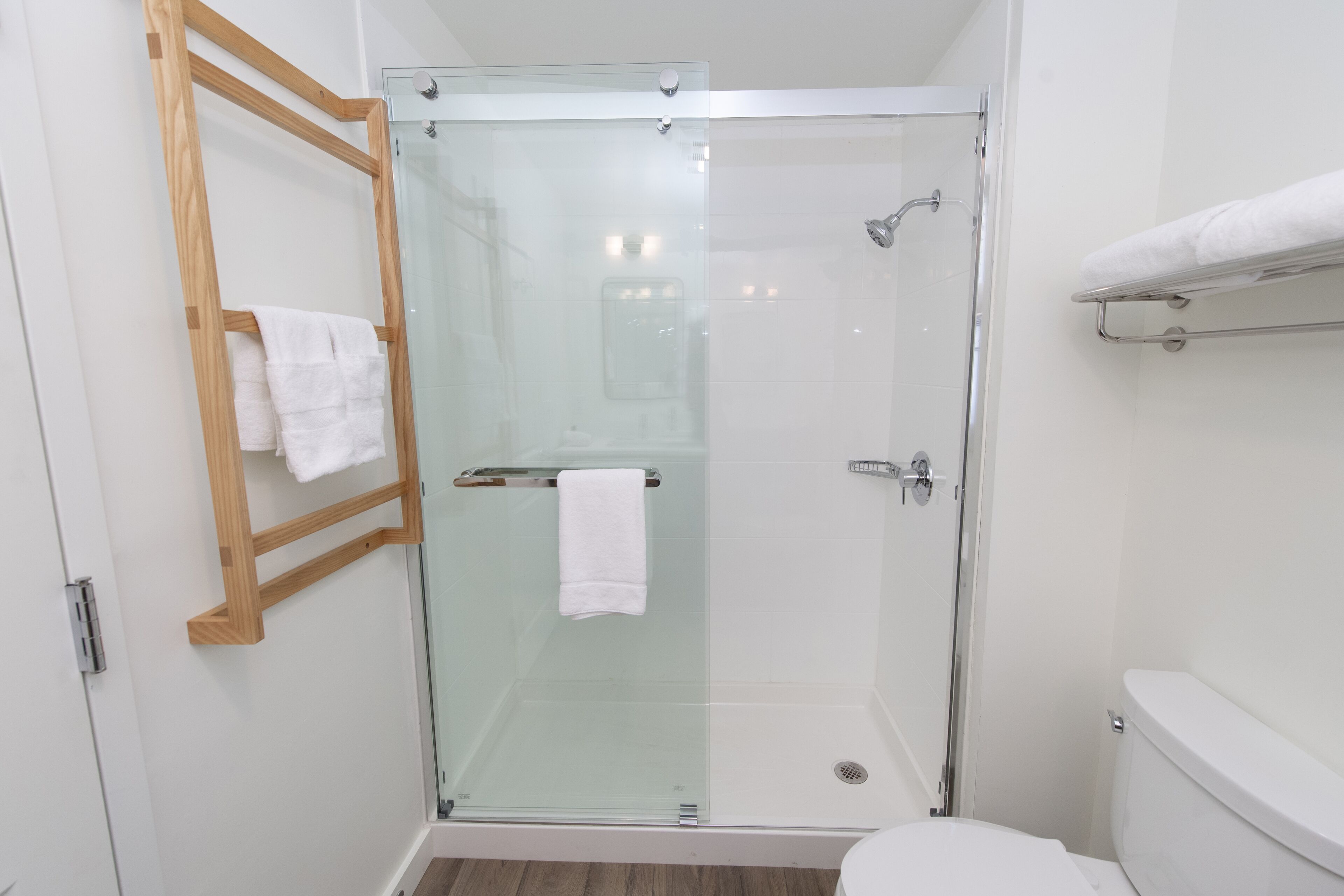 Une salle de bain moderne avec une douche à parois de verre, un porte-serviettes en bois et des toilettes blanches.
