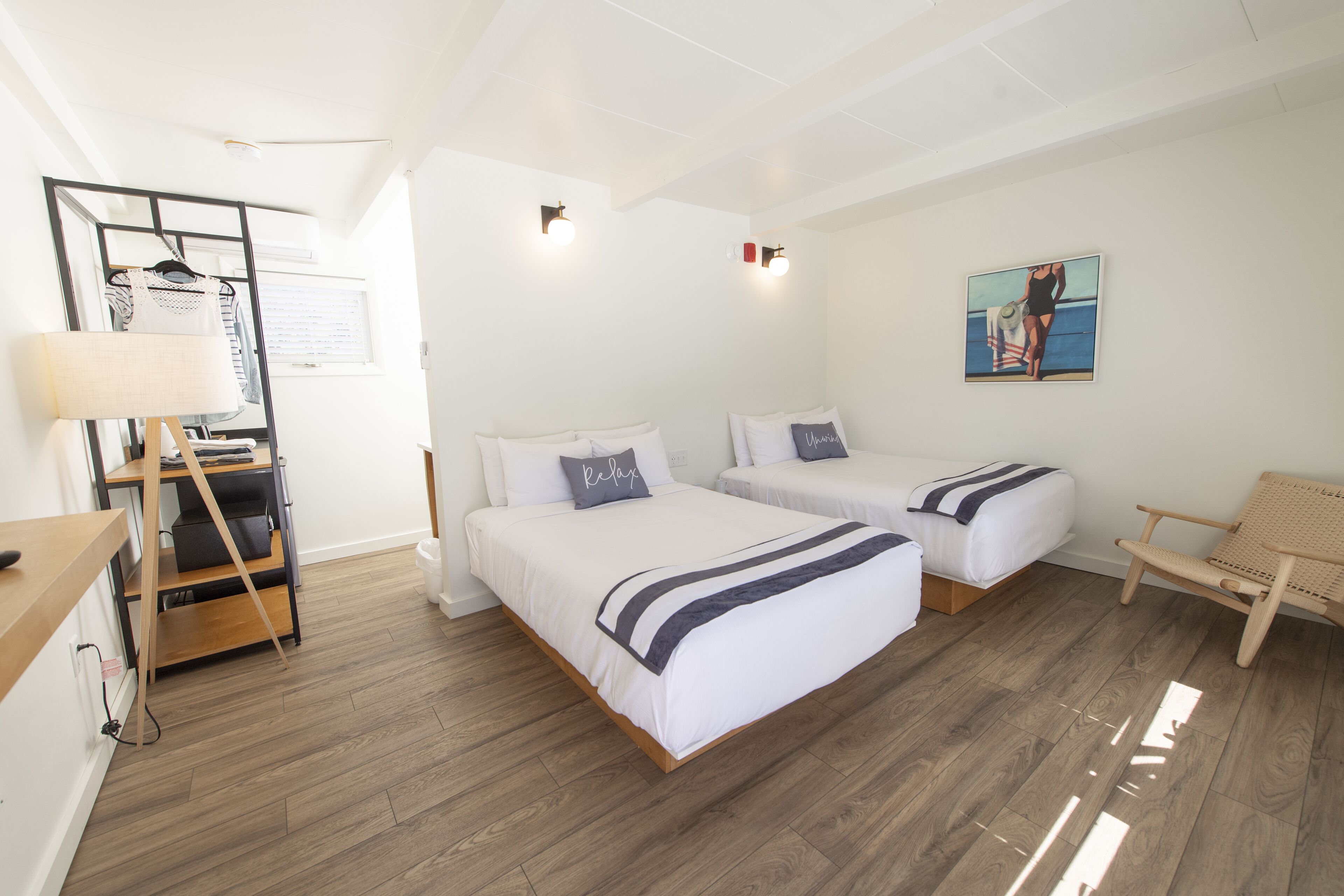 A hotel room with two beds, a desk, a chair, and a painting on the wall.
