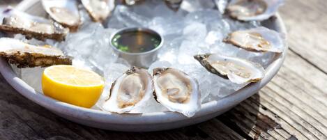 A plate of oysters on ice with a lemon wedge and a small bowl of sauce.