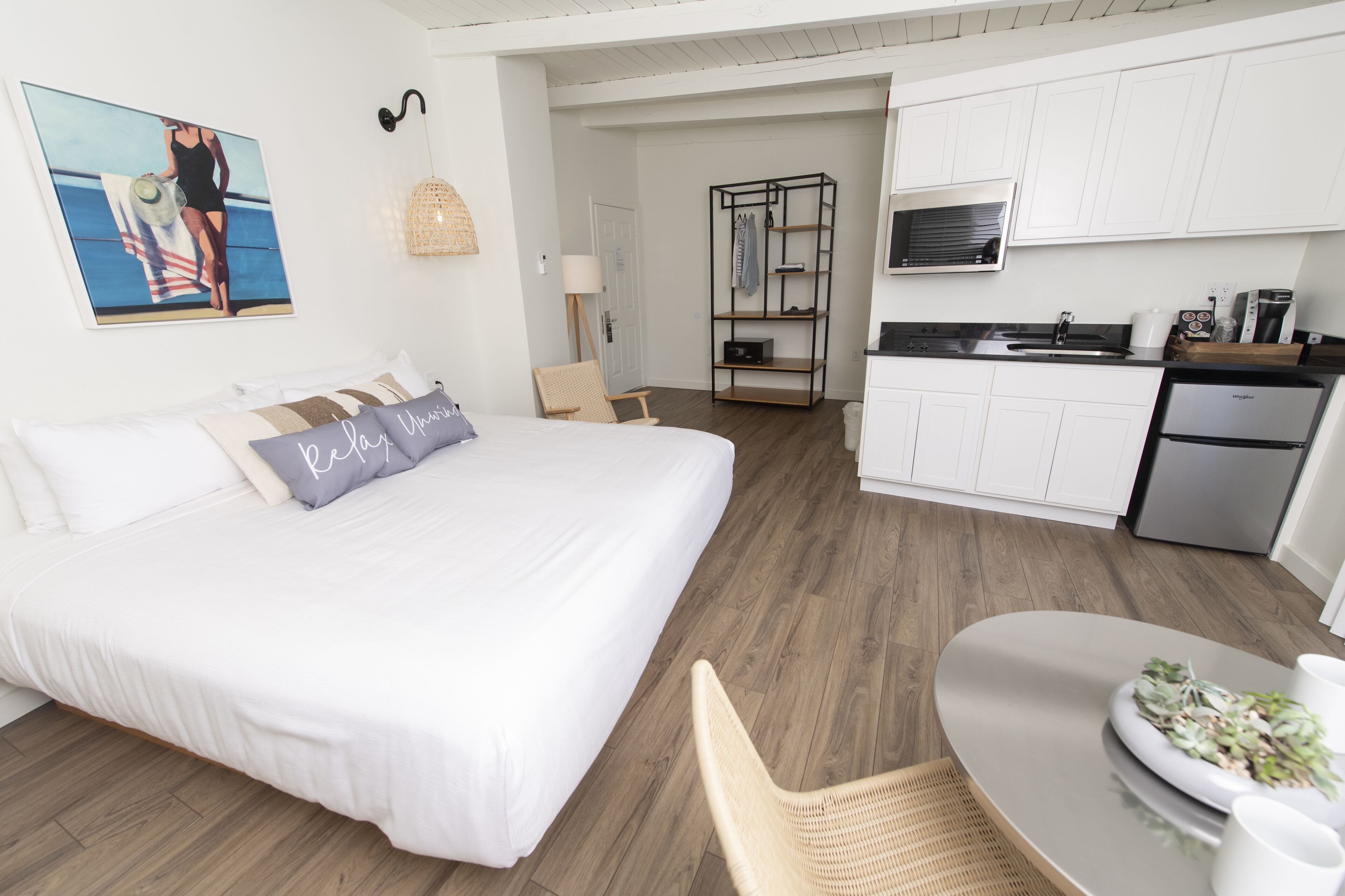 Quarto de hotel moderno com uma cama grande, uma mesa de jantar, área de cozinha e vista para o oceano.