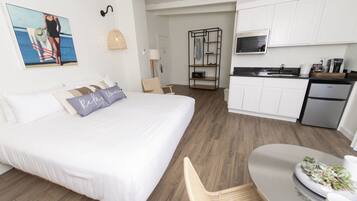 Quarto de hotel moderno com uma cama grande, uma mesa de jantar, área de cozinha e vista para o oceano.