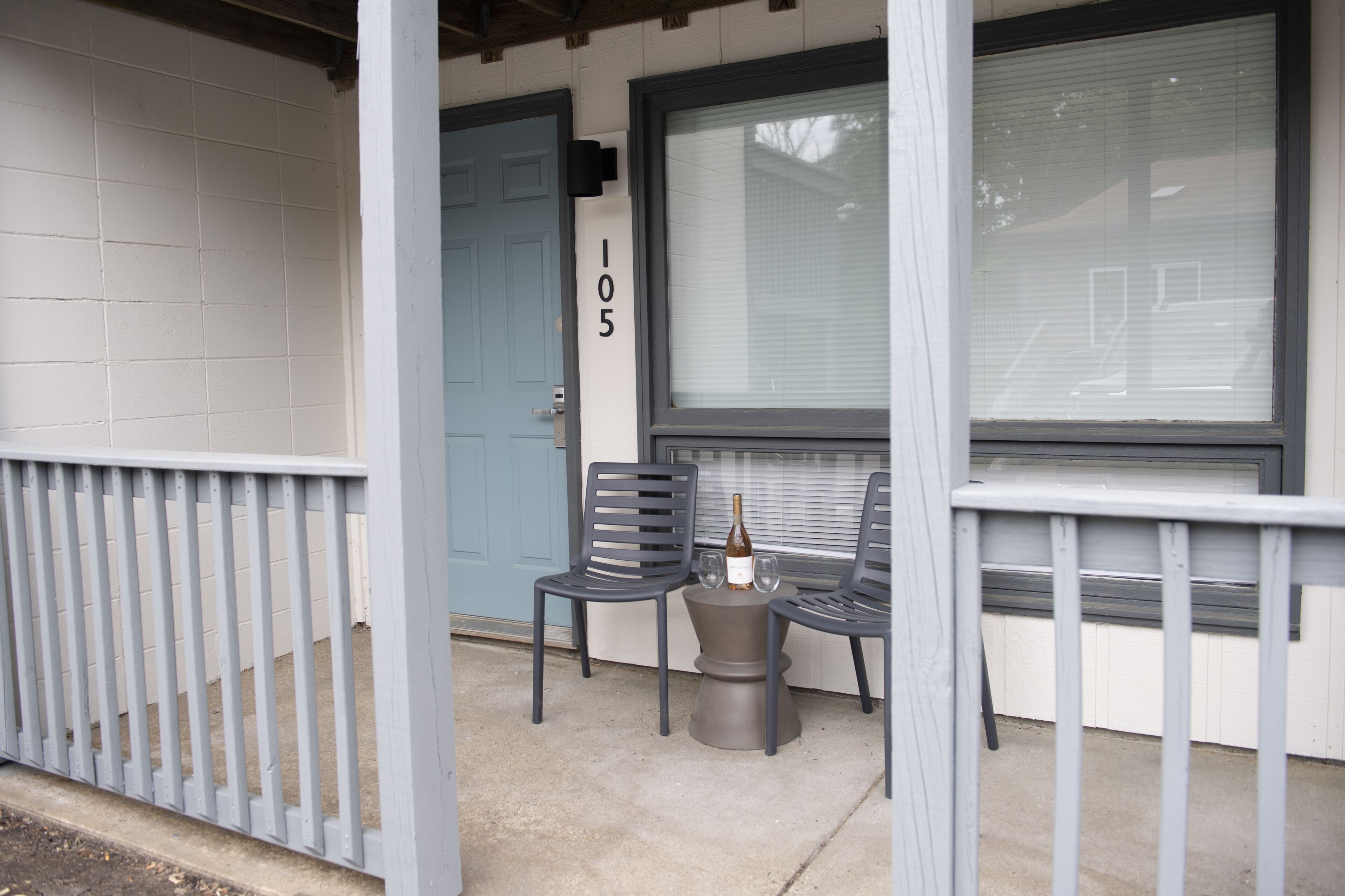 A porch with two chairs, a small table, and a bottle of wine.