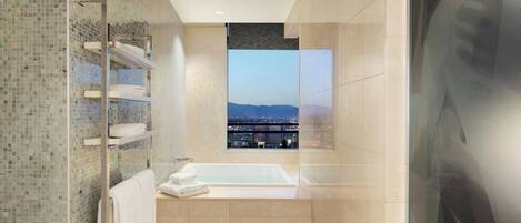 Un baño moderno con una cabina de ducha de vidrio, una bañera y vistas a un paisaje urbano a través de un amplio ventanal.