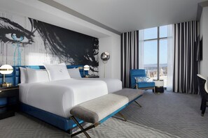 A modern hotel room with a large bed, a bench, a desk, and a view of the city.