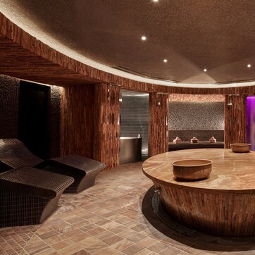 A spa area with a wooden reception desk, a large circular basin, and a stone pedestal with a vase.