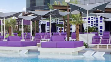 Ein Poolbereich mit violetten Liegestühlen und Sonnenschirmen, einem klaren blauen Pool und einem modernen Gebäude im Hintergrund.