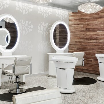 A modern bathroom with two vanity sinks, each with a round mirror and under-cabinet lighting. The wall features a wooden panel design, and the floor is covered with speckled tiles.