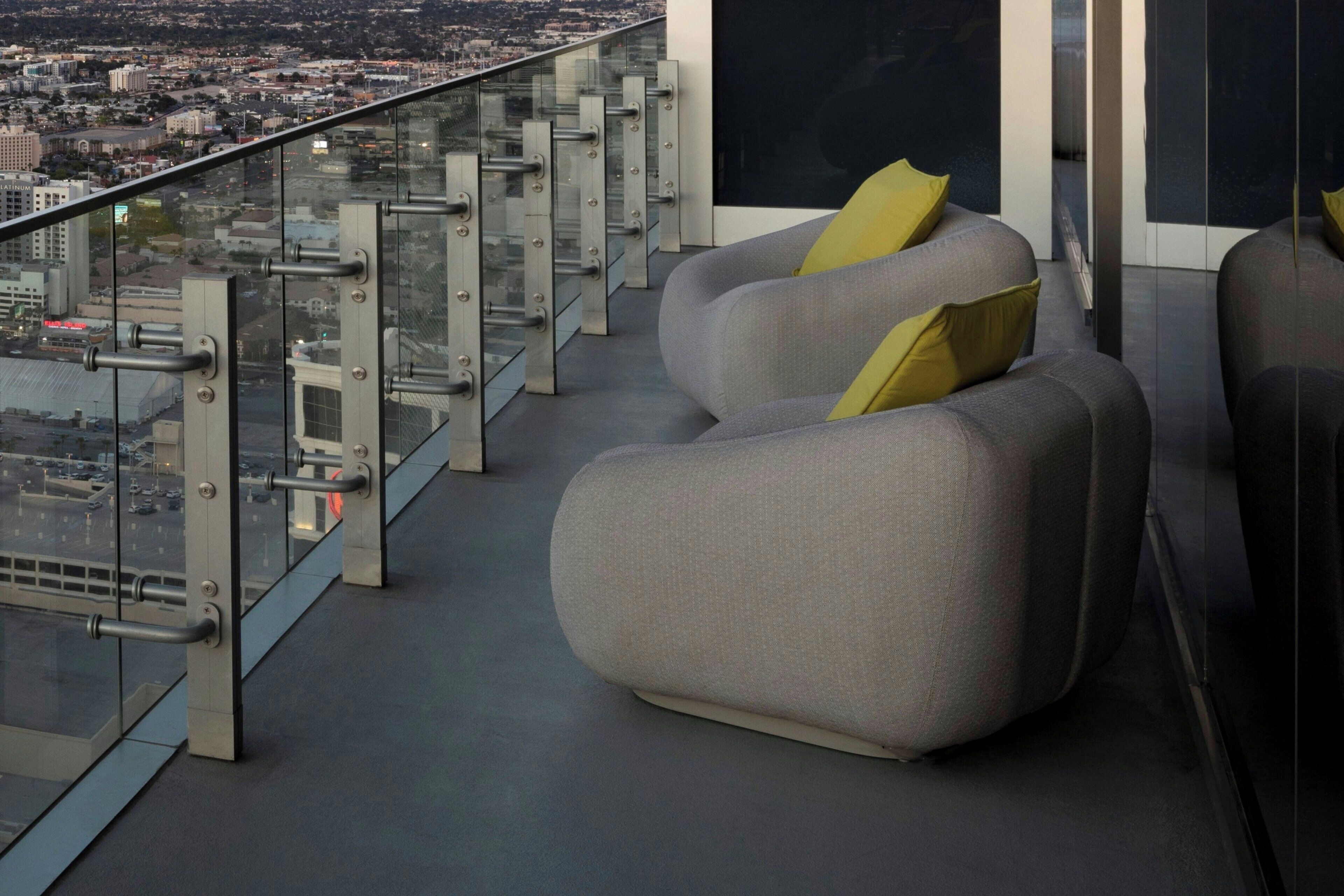 Un salón moderno con vista a la ciudad, que cuenta con barandilla de vidrio y asientos contemporáneos.