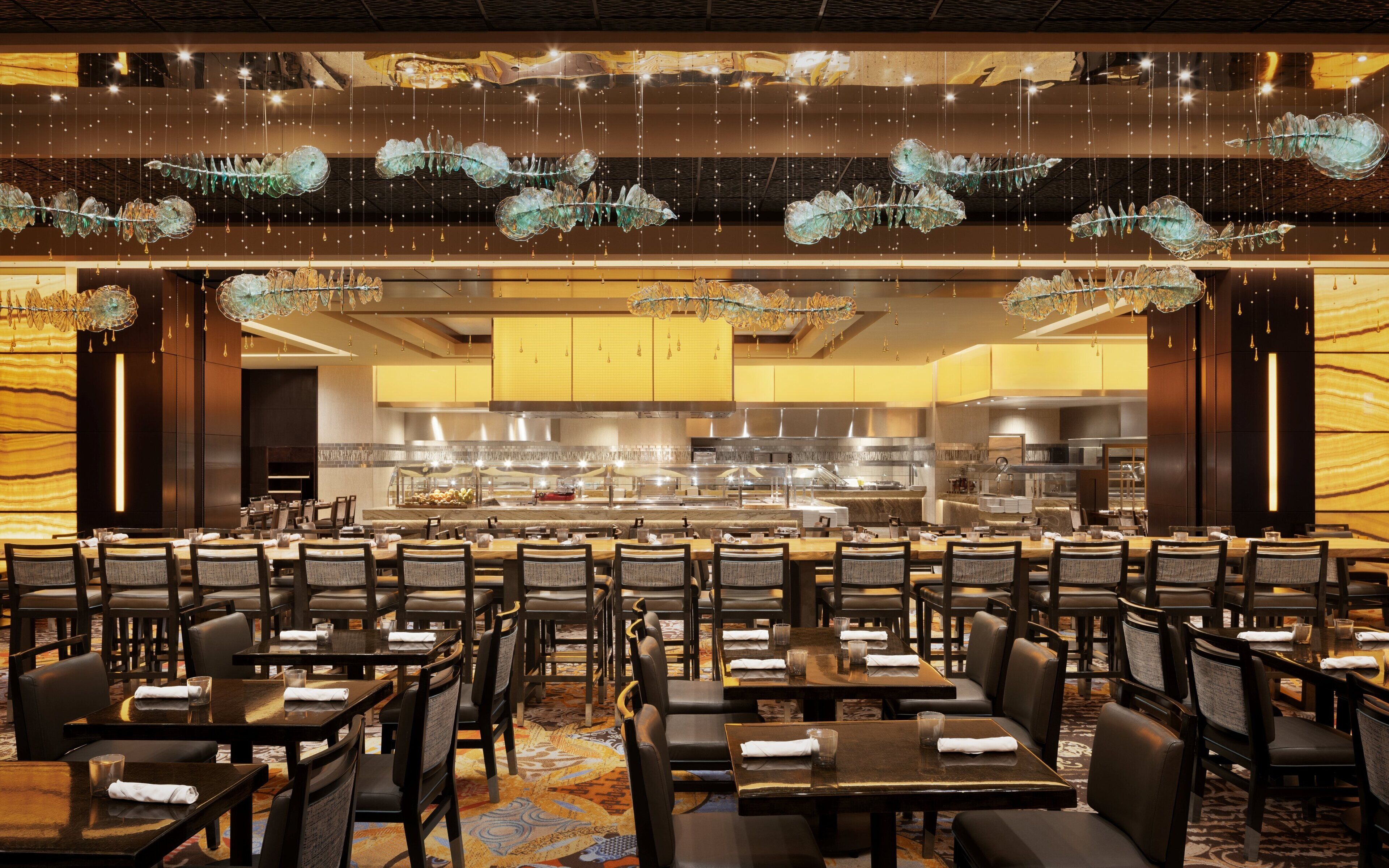 A spacious dining area with multiple tables and chairs, a central kitchen area, and decorative hanging elements.