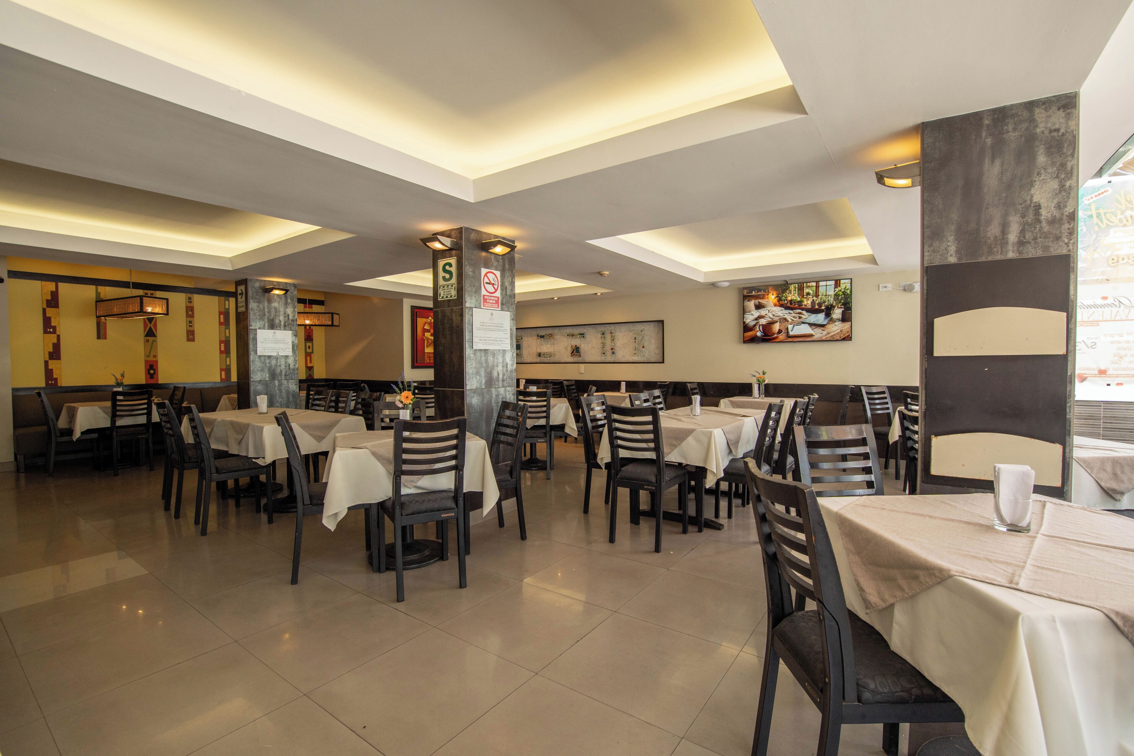 A restaurant with multiple tables and chairs, ceiling lights, and wall decorations.