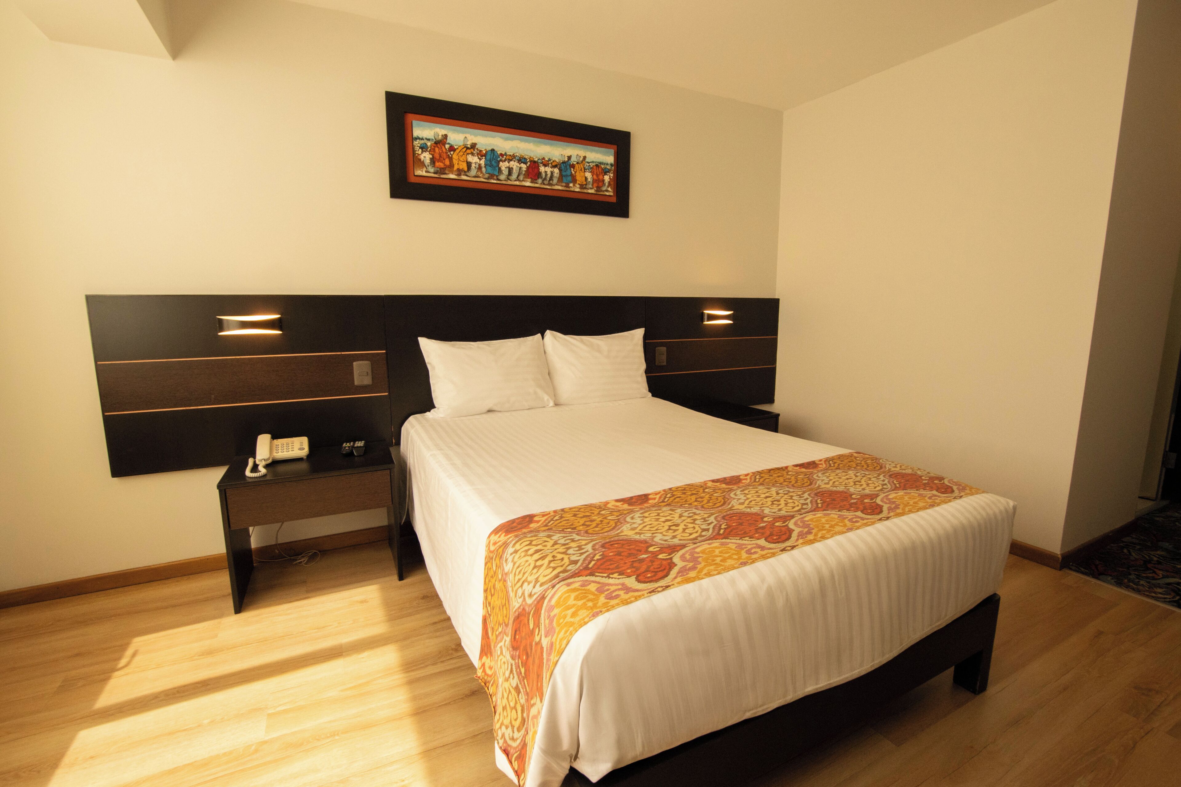 A hotel room with a bed, bedside tables, a telephone, and a painting on the wall.
