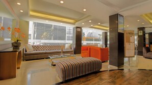 A modern lobby with a sofa, ottoman, and a reception desk. - Britania Miraflores (Lima)