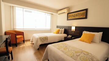 A hotel room with two beds, a desk, a chair, and a large window.