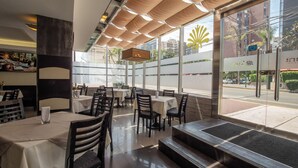A restaurant with tables and chairs, large windows, and a view of the street. - Britania Miraflores (Lima)