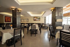 Un restaurante con varias mesas y sillas, un techo con iluminación empotrada y obras de arte en las paredes.