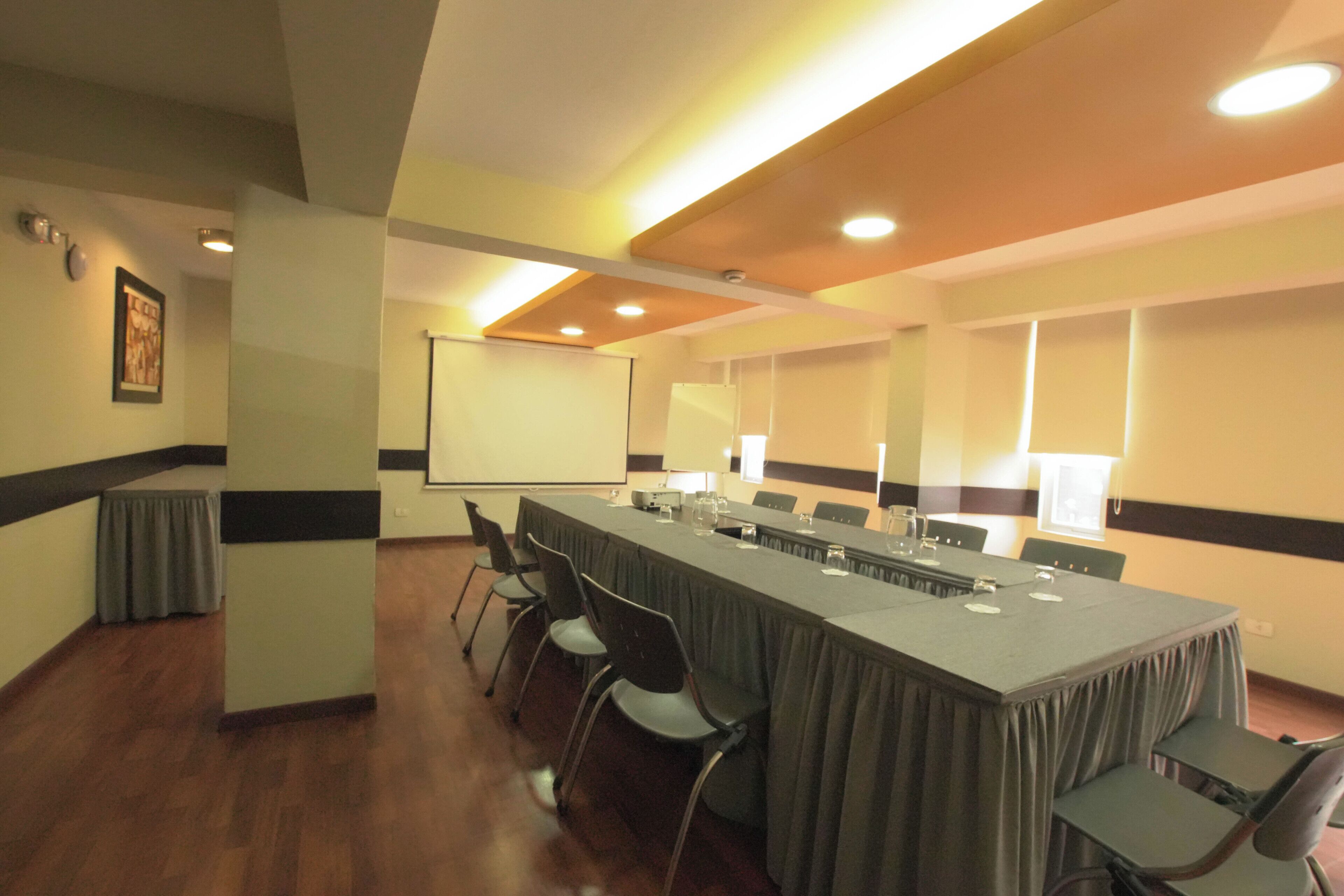A conference room with a long table, chairs, a projector screen, and a whiteboard.