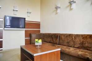 A modern living room with a brown leather sofa, a wooden coffee table with a glass vase, and a flat-screen TV mounted on the wall.