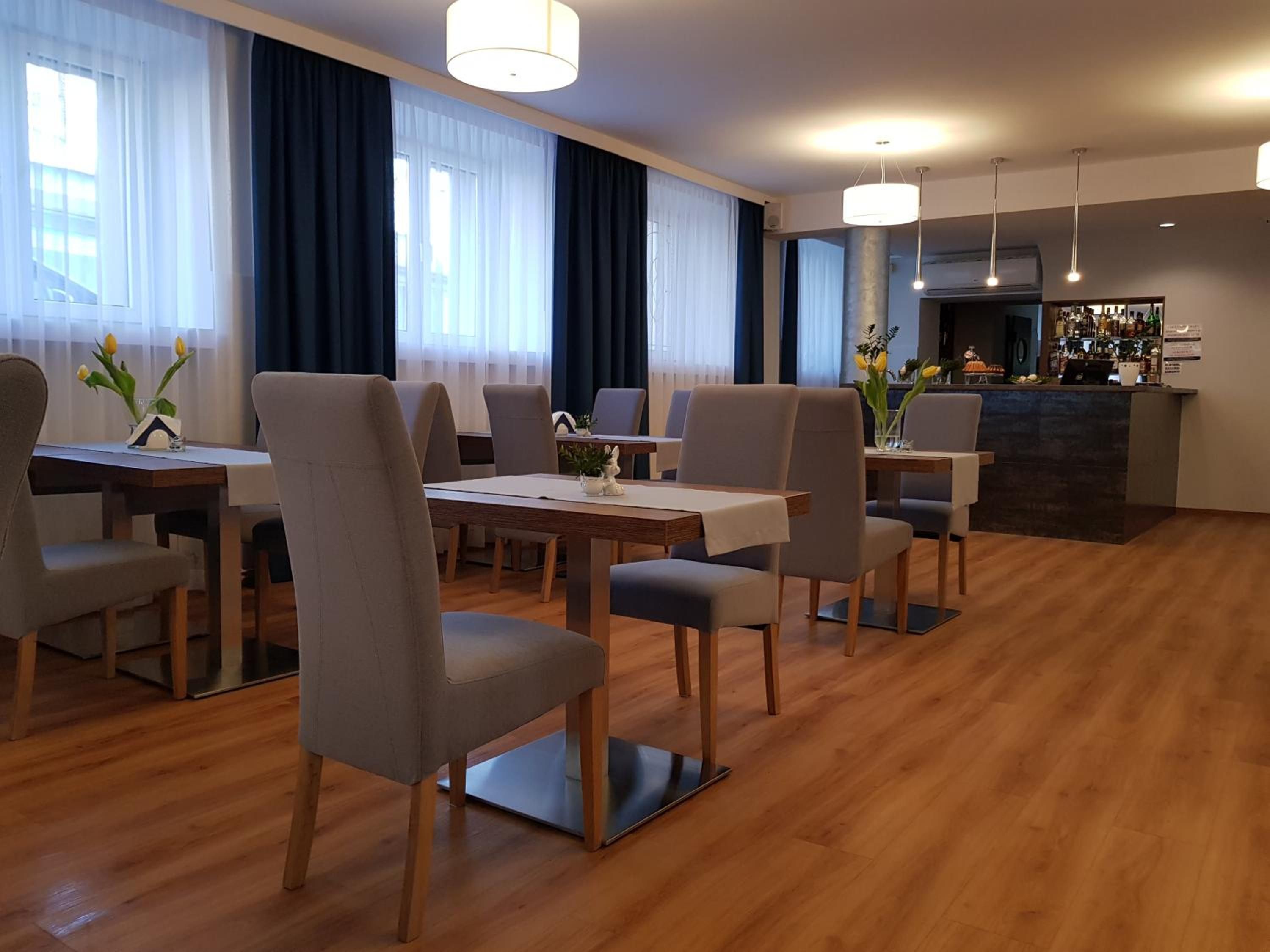 A hotel dining area with wooden flooring, modern chairs, and a bar counter with a variety of bottles.