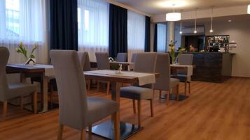 A hotel dining area with wooden flooring, modern chairs, and a bar counter with a variety of bottles.