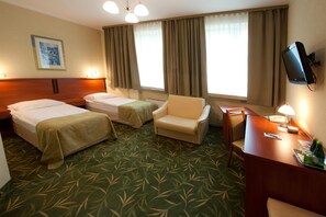 A hotel room with two single beds, a sofa, a desk with a lamp, and a television.