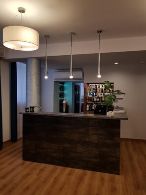 A reception area with a central counter, pendant lighting, and a bar stocked with bottles.