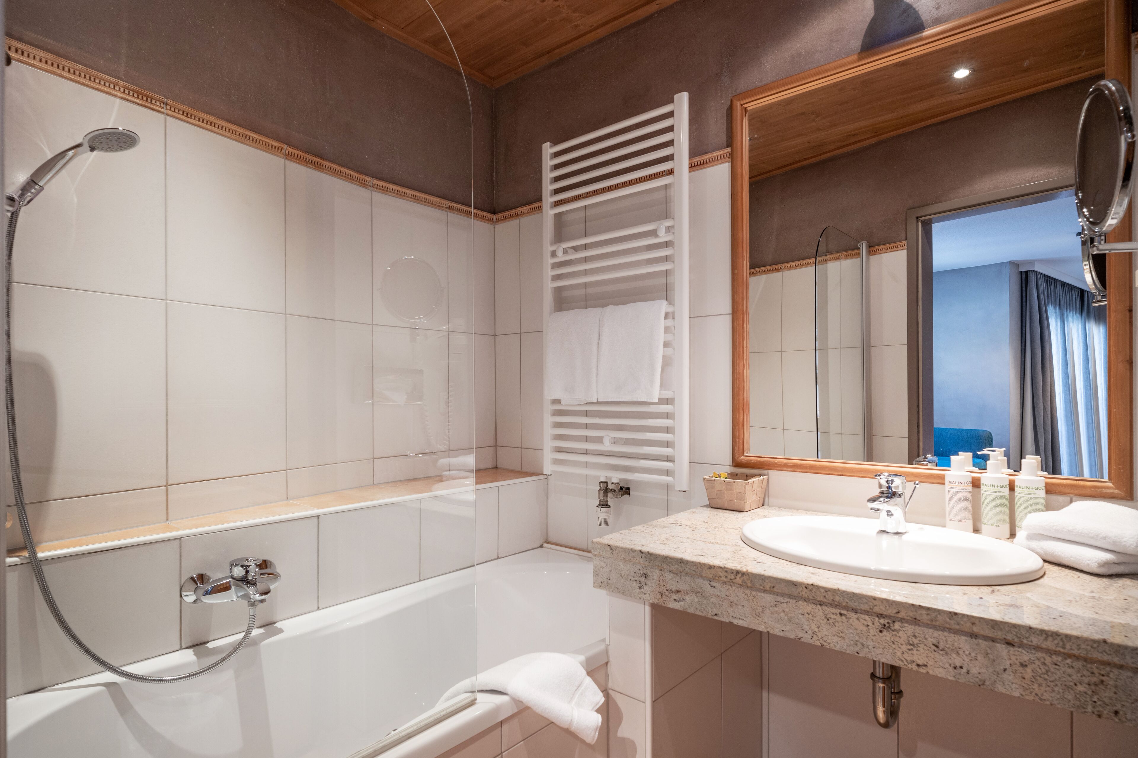 Un baño moderno con bañera, ducha, lavabo con artículos de aseo y espejo.