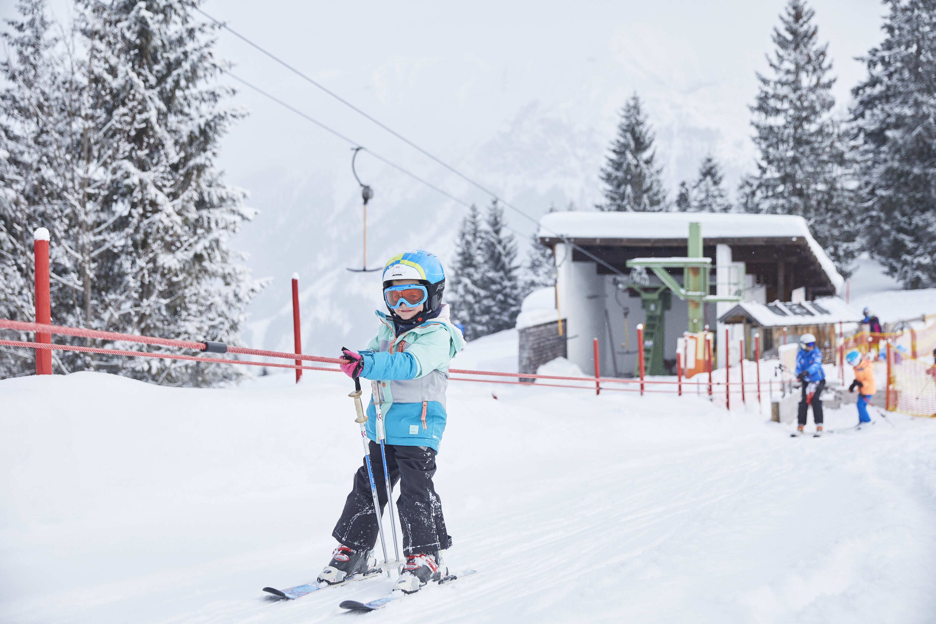 Une piste de ski avec un enfant qui skie, un télésiège et un chalet en arrière-plan.
