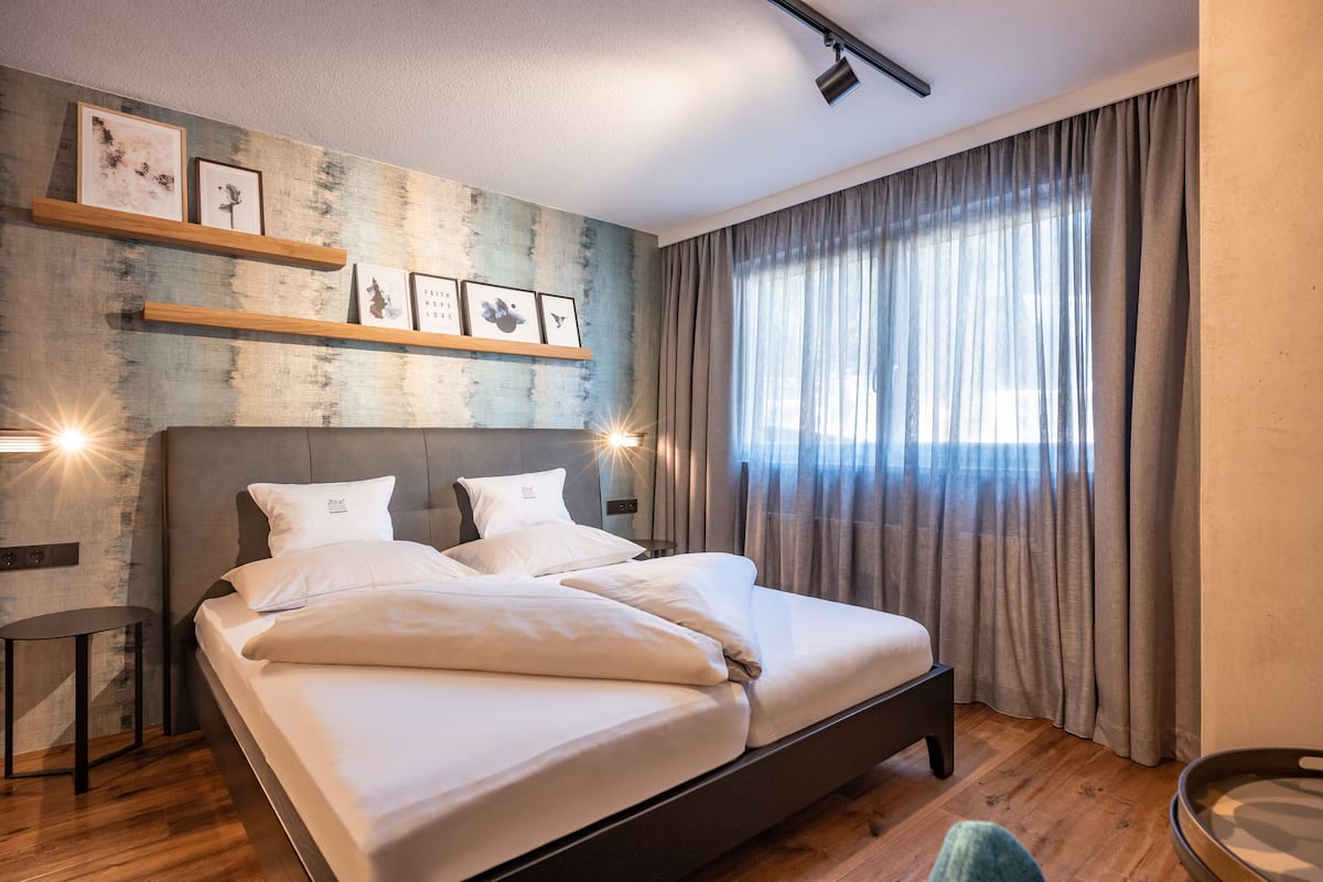A modern bedroom with a large bed, wooden floor, and a wall with framed pictures.